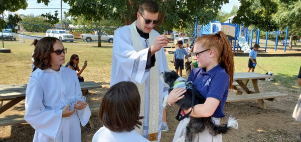 A priest blesses a dog held by a girl
