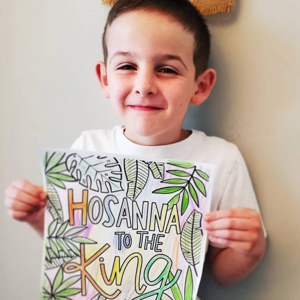 A boy holds a coloring sheet reading Hosanna to the King