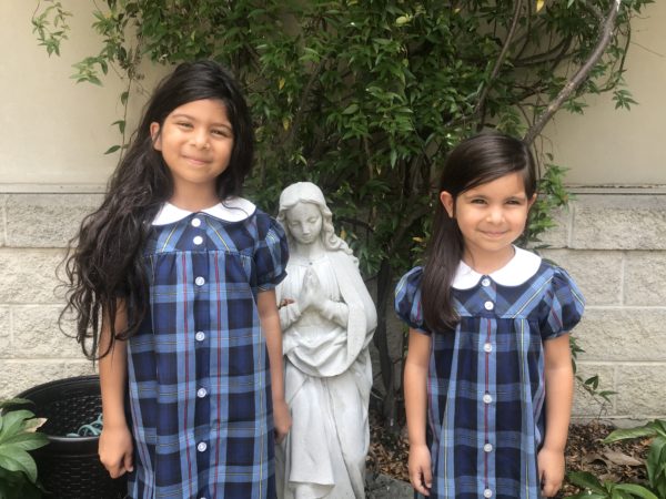 Two girls in uniforms next to a saint statue