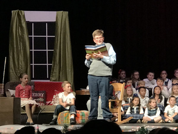A boy reads from a book onstage