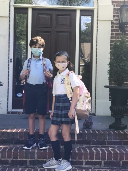 A boy and girl in uniforms with backpacks and masks